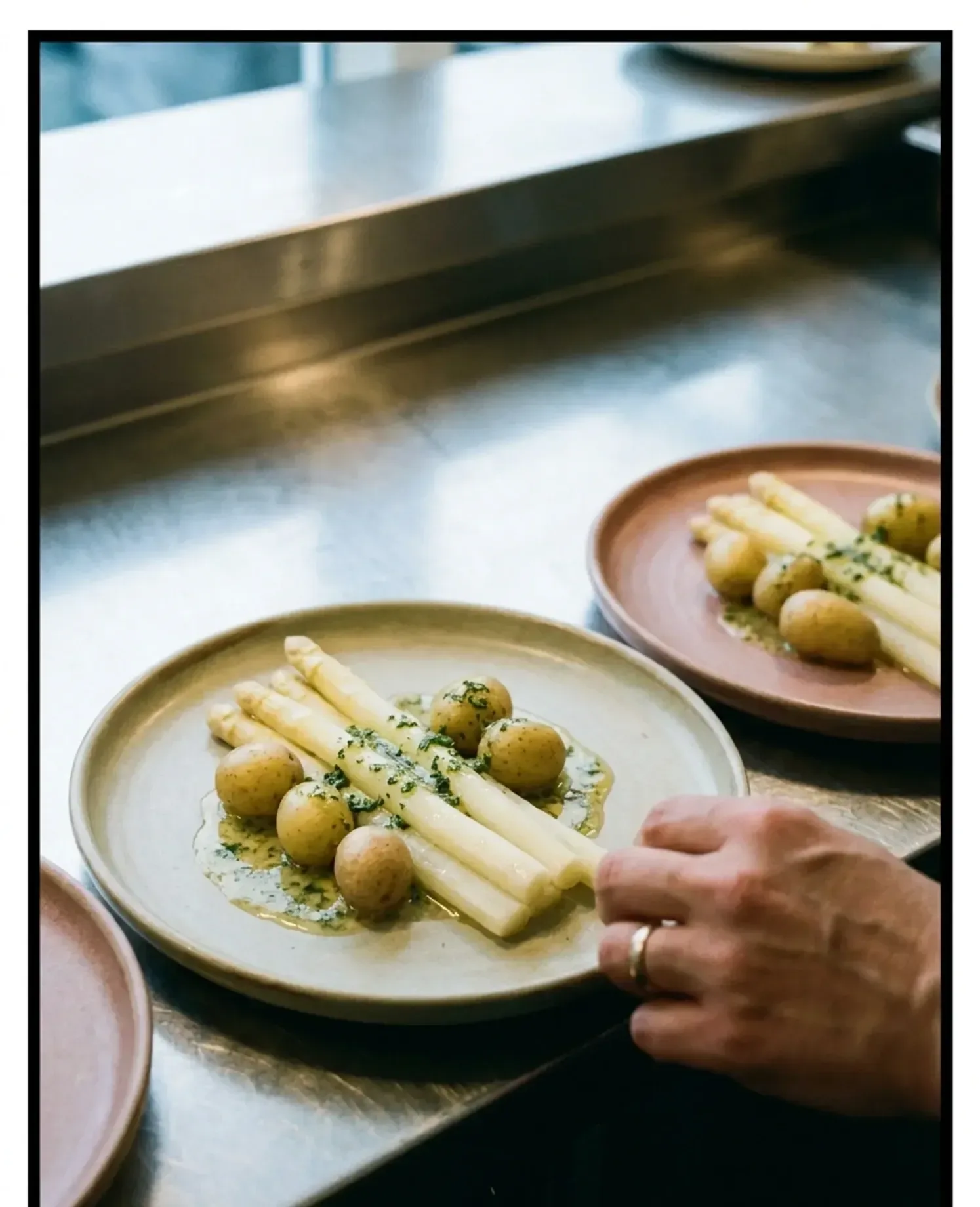 Een kok schuift een bord met witte asperges en krieltjes over de doorgeefbalie.